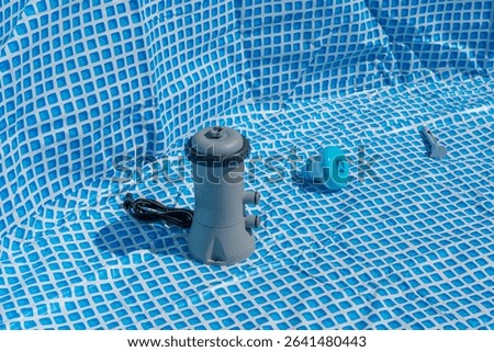 Setting up a pool with pump and accessories on a blue and white patterned surface. The individual parts are ready for assembly.