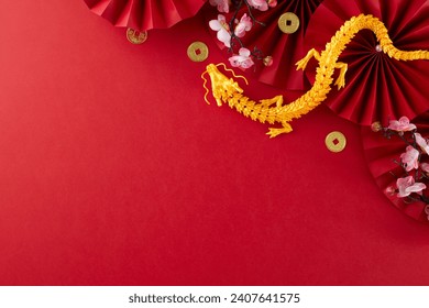 Setting the stage for a festive Lunar New Year 2024. Top view photo of gold dragon, folding fans, traditional coins, sakura bloom on red background with advert zone