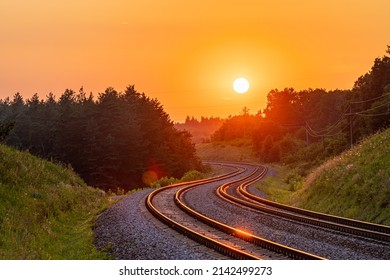 The setting sun against the background of the international railway line passing through the forest. Sunset lighting. Winding road. Railway infrastructure.
