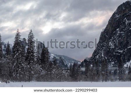 The setting sun is barely breaking through the clouds in a snow-covered Yosemite valley, on a late winter afternoon.