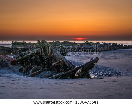 Setting sun behind an exposed shipwreck at low tide from World War II at the beach