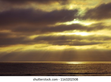 As The Setting Sun Breaks Through A Small Hole In The Atmosphere And Thick Clouds, A Spotlight Appears On The Pacifc Ocean And The Particles Of Light Spread Out In An Angelic, Godly Display Of Beauty