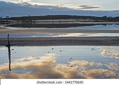 Setting sun, causing reflections of clouds in a salt lake, wheat belt of Western Australia.Reflections galore, three layers of lake water, reflecting clouds and an old fence.