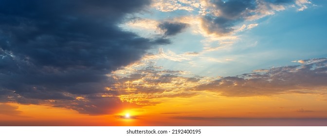 Setting sun in the orange blue evening sky. Sun rays break through the light clouds at sunset. Dark stormy cloud covering half the sky at sundown. Picturesque skyscape wide panorama. Weather forecast.