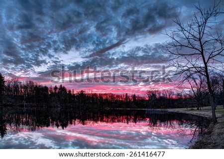 The setting sun paints the sky with vivid and dramatic colors that is reflected on a small Indiana pond in Sodalis Nature Park. Stock photo © 