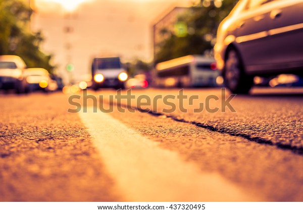 Setting sun in the suburbs, the cars driving on\
road. View from the level of the dividing line, image in the\
orange-purple toning