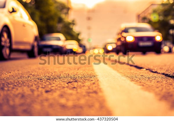 Setting sun in the suburbs, the cars driving on\
road. View from the level of the dividing line, image in the\
orange-purple toning