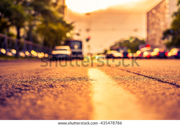 Setting sun in the suburbs, stream of cars\
traveling on the road. View from the level of the dividing line,\
image in the orange-purple\
toning