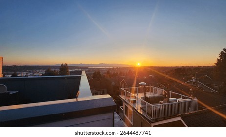 Setting sun with visible sunrays highlight a serene rooftop roofdeck with pergola near Woodland park in Seattle Washington with view of the ocean and bay, clear blue skies with orange sunset