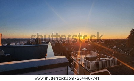 Setting sun with visible sunrays highlight a serene rooftop roofdeck with pergola near Woodland park in Seattle Washington with view of the ocean and bay, clear blue skies with orange sunset