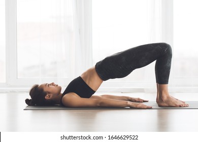 Setu Bandhasana. Young attractive woman in sportswear doing glute bridge pose, exercising on gray yoga mat, copyspace - Shutterstock ID 1646629522