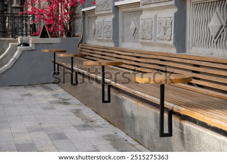 The setup consists of a long row of sturdy wooden benches that have tables affixed to them, offering both a practical and visually attractive arrangement for numerous outdoor or communal spaces