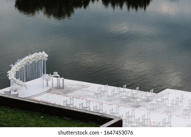 Setup wedding ceremony on pier. Wedding arch decorated with flowers and white chairs for guests. Wedding atmosphere, scenery, celebration. Photography, concept. Top view from the sky.