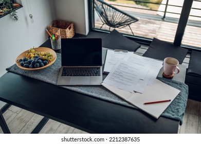 Setup for work at home on the table with some documents and laptop. Working remotely from home. Black table with a coffee cup on it. Copy space.