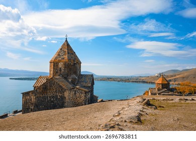 A Sevan Monastery Sevanavank church is on a hill overlooking a body of water. The sky is clear and the sun is shining