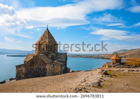 A Sevan Monastery Sevanavank church is on a hill overlooking a body of water. The sky is clear and the sun is shining