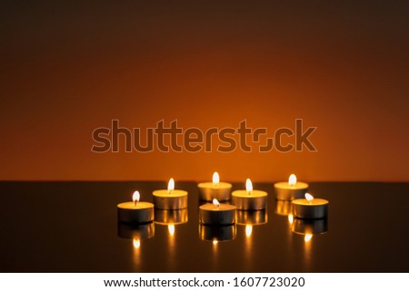seven candles burning on a shiny black surface and orange ackground