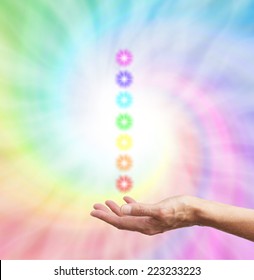 The Seven Chakras  -  healer's hand  palm up with a stack of chakra star bursts on a rainbow spiral background