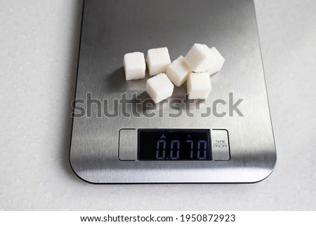 Seven lumps of refined sugar are weighed on a kitchen scale. Diet.