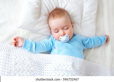 Seven month old baby sleeping on white blanket and pillow. Sleepy child on soft bedding with pacifier