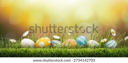 Seven painted easter eggs celebrating a Happy Easter on a spring day with a green grass meadow, bright sunlight and a warm oranged coloured background with copy space.