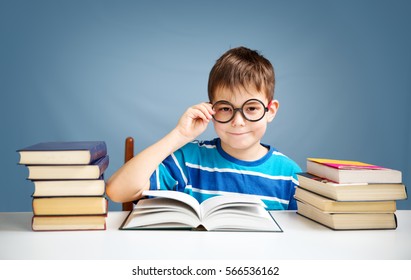 seven years old child reading a book at home. Boy studying at table on blue background