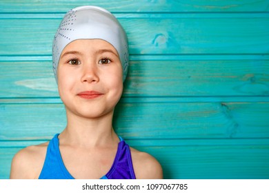 A Seven-year-old Girl In A Blue Swimsuit And A Swimming Cap Against A Blue Wooden Wall