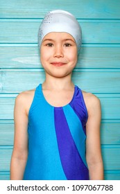 A Seven-year-old Girl In A Blue Swimsuit And A Swimming Cap Against A Blue Wooden Wall