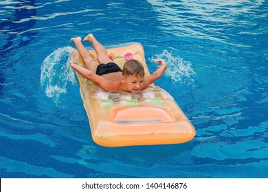 seven-year-old tanned child swims on an inflatable mattress in the outdoor pool . Children and summer. Rowing hands in the water - Shutterstock ID 1404146876