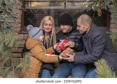 Several Adult Family Members Give Presents To A Cute Little Boy Outside. Boy Is Happy And Smiling