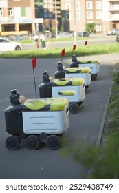 Several autonomous delivery robots line up on a city street, each displaying the Yandex logo. The robots are parked near a sidewalk, with a blurred city background.