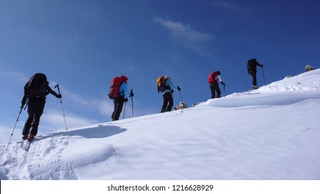 several backcountry skiers hike and climb to a remote moutain peak in Switzerland on a beautiful winter day - Powered by Shutterstock