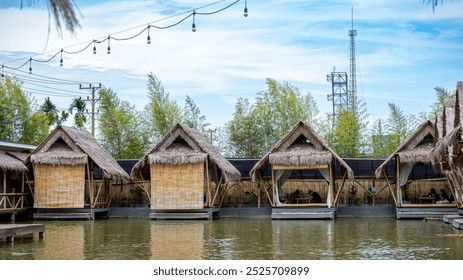 several bamboo huts floating on a pond, surrounded by lush greenery, with a clear blue sky in the background. - Powered by Shutterstock