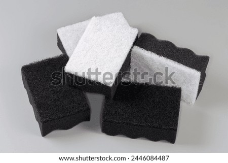 Several black and white kitchen soft synthetic cleaning sponges with hard urethane abrasive layer on a gray background
