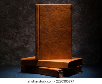 several books with the same binding on a dark background isolated. three books with a brown cover without inscriptions and titles with free space for text