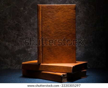 several books with the same binding on a dark background isolated. three books with a brown cover without inscriptions and titles with free space for text