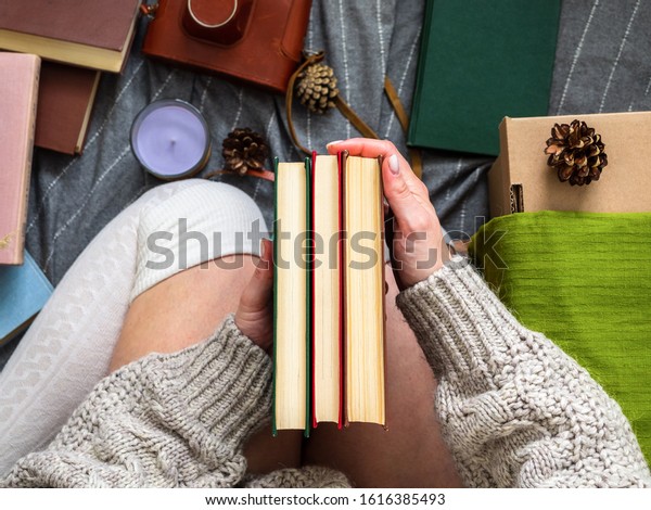 Several books in women\'s hands. A girl in\
a knitted sweater is surrounded by many\
books.