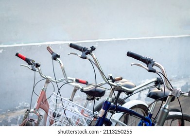 Several classic bicycles are parked near the wall of the building. In the frame, the upper part of the bicycles is the handlebar, saddle, basket. Selective focus.