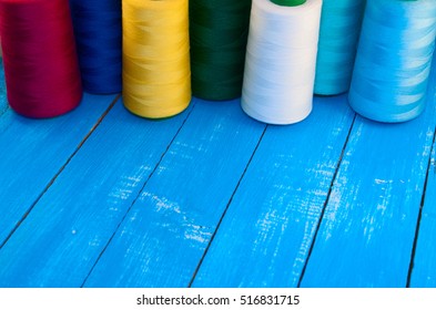 Several of colored spools of thread for sewing and embroidery on a blue wooden table, empty space
