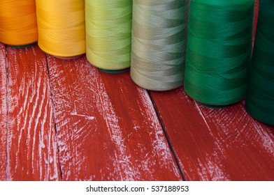 Several of colored spools of thread for sewing and embroidery on a red wooden table