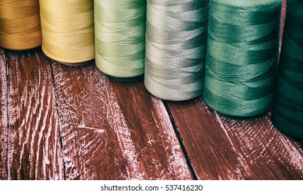 Several of colored spools of thread for sewing and embroidery on a red wooden table , vintage toning