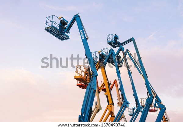 Several colorful aerial work platforms\
(AWP) or elevating work platforms (EWP) against the sunset blue sky\
drawback. Industrial machines on hold\
concept.