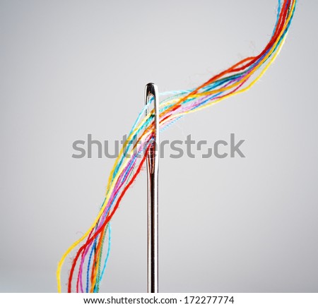 Several colourful threads in a needle.