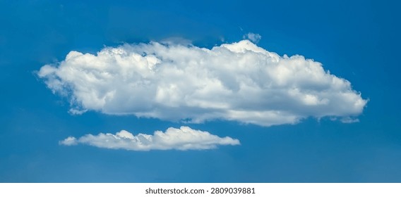 Several cumulus clouds. Cloud flowing lazily like cottony fibers against a clear, serene blue background. The sky speaks of calm, peace, and silence.