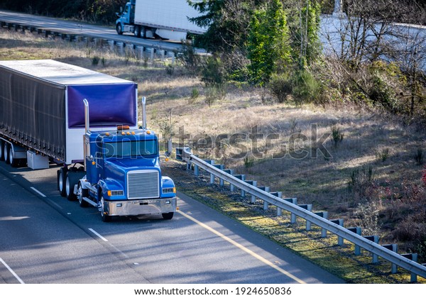 Several different big rigs semi trucks with dry van semi\
trailers running on the divided highway road with one way traffic\
lines moving in opposite directions for delivery of goods to\
recipients 