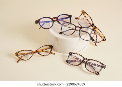 several different fashion eyeglass frames, glasses on ceramic podium, creative presentation of eyeglasses beige background