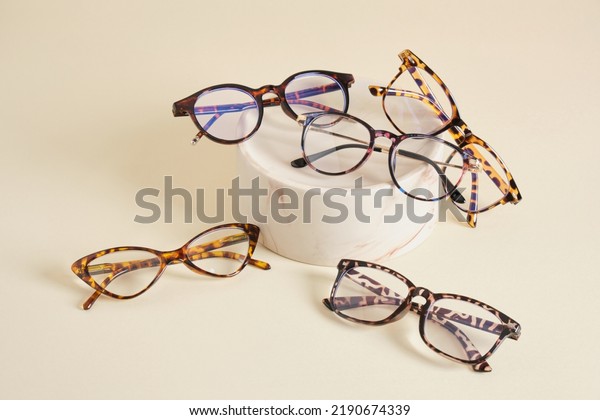 several different fashion eyeglass frames,\
glasses on ceramic podium, creative presentation of eyeglasses\
beige background