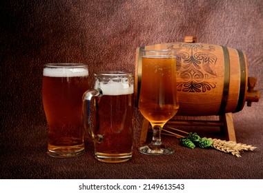 Several Different Glasses With Light Beer, A Wooden Keg, Ears Of Wheat And Hops On A Brown Abstract Background. Close-up.