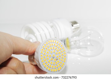 Several different led bulbs and compact fluorescent lamps and the male hand on a light background.