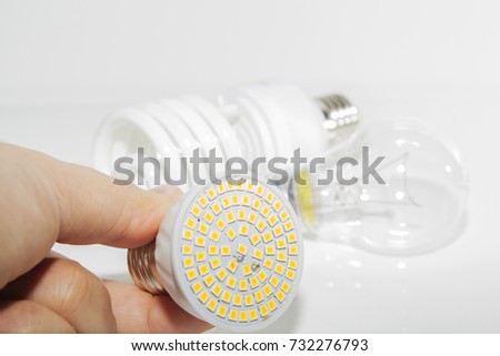 Several different led bulbs and compact fluorescent lamps and the male hand on a light background.